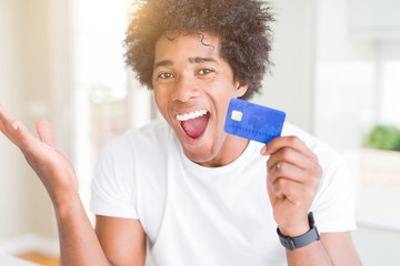African American man holding credit card very happy and excited, winner expression celebrating victory screaming with big smile and raised hands
