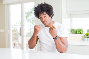 Young african american man wearing casual white t-shirt sitting at home Ready to fight with fist defense gesture, angry and upset face, afraid of problem