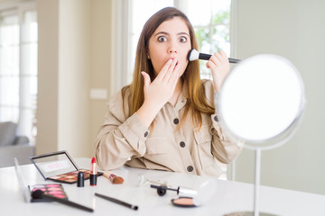 Sticker - Beautiful young woman using make up cosmetics applying color using brush cover mouth with hand shocked with shame for mistake, expression of fear, scared in silence, secret concept