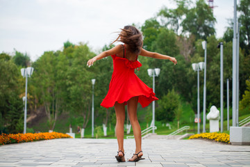 Wall Mural - Young beautiful woman in red dress walking on the summer street