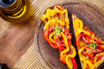 Top view on bruschetta with red, yellow baked, roasted bell pepper, olive oil on wooden cutting board on wooden background. Fresh italian homemade cuisine. Copy space. Two tasty bruschetta. Vegan food