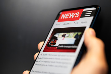 A man holding mobile smart phone with news on screen. Newspaper online portal in browser.