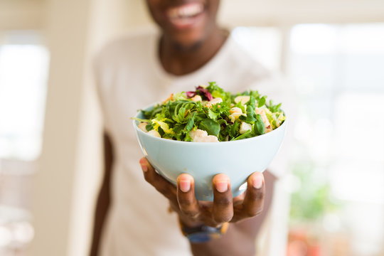 african young man holding a bowl of healthy salad smiling cheerful