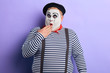 Shocked funny mime artist standing in disbelief closing his mouth with a palm isolated on blue background. close up portrait. studio shot.copy space