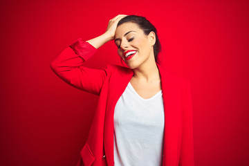 Young beautiful business woman standing over red isolated background smiling confident touching hair with hand up gesture, posing attractive and fashionable