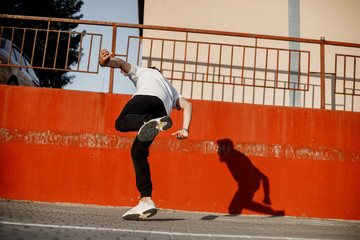 Wall Mural - Young guy dressed in jeans and white t-shirt is dancing modern dance in the street against a painted concrete wall in the sunny day