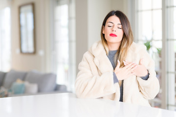 Sticker - Young beautiful woman wearing winter fur coat at home smiling with hands on chest with closed eyes and grateful gesture on face. Health concept.