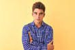 © Krakenimages.com - Young handsome man wearing casual shirt standing over isolated yellow background skeptic and nervous, disapproving expression on face with crossed arms. Negative person.
