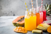 Glasses Of Tasty Fresh Tropical Juices With Fresh Tropical Fruits, Papaya Pine Apple Mango Dragon On Gray Background.