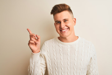 Young handsome man wearing winter sweater standing over isolated white background with a big smile on face, pointing with hand and finger to the side looking at the camera.