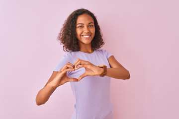 Wall Mural - Young brazilian woman wearing t-shirt standing over isolated pink background smiling in love doing heart symbol shape with hands. Romantic concept.