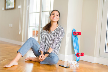 Poster - Young woman sitting on the floor using skateboard and headphones looking away to side with smile on face, natural expression. Laughing confident.