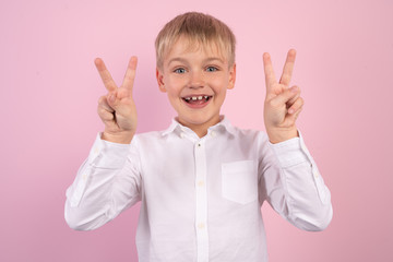 Wall Mural - Close up photo little age beautiful boy hold arm show victory sign say hi to friends relatives positive optimistic wear white shirt isolated pink bright vibrant vivid background