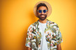 © Krakenimages.com - Indian man on vacation wearing floral shirt hat sunglasses over isolated yellow background with a happy and cool smile on face. Lucky person.