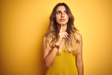 Sticker - Young beautiful woman wearing t-shirt over yellow isolated background Thinking concentrated about doubt with finger on chin and looking up wondering