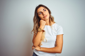 Sticker - Young beautiful woman wearing casual white t-shirt over isolated background with hand on chin thinking about question, pensive expression. Smiling with thoughtful face. Doubt concept.