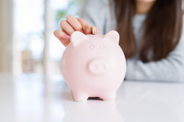 Wall Mural - Young woman putting a coin inside piggy bank as savings for investment