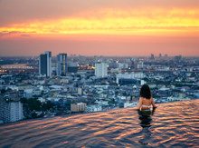 Young Woman Relax In Swimming Pool On Roof Top During Amazing Sunset And Enjoy Cityscape