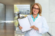 © elnariz - Female doctor smiling, holding optimistic results of diagnosis on clipboard, blank card for print, copy space for text