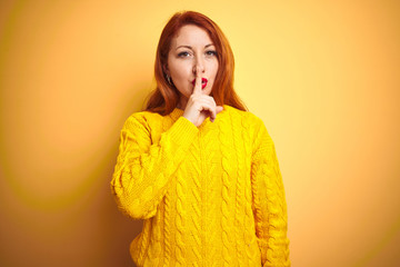 Canvas Print - Beautiful redhead woman wearing winter sweater standing over isolated yellow background asking to be quiet with finger on lips. Silence and secret concept.