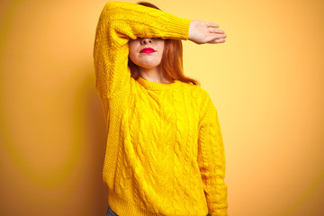 Poster - Beautiful redhead woman wearing winter sweater standing over isolated yellow background covering eyes with arm, looking serious and sad. Sightless, hiding and rejection concept