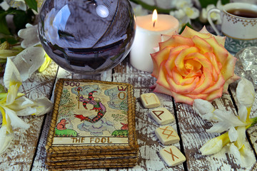 Tarot cards deck, crystal ball, runes and flowers on witch table.