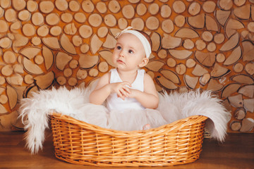 girl in a dress sitting in a basket on a white firewood. the concept of holiday, fun, home comfort