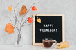 Happy Wednesday text on black letter board and bouquet of branches with yellow leaves on clothespins in vase on table Template for postcard, greeting card Concept Hello autumn Wednesday