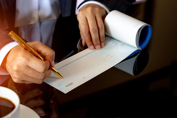 Wall Mural - Business woman hand writing and signing checkbook on the wooden table at office. Paycheck or payment by cheque concept.