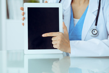 Wall Mural - Female doctor using tablet computer while sitting at the workplace, close-up of hands. Medicine, healthcare and help concept