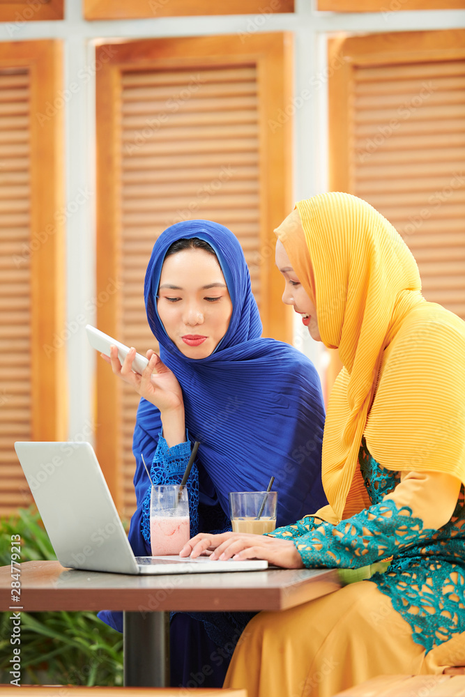 Pretty young muslim woman in hijabs talking and typing on laptop when ...