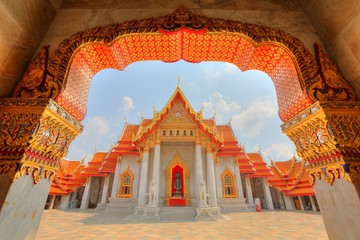 View through the gate to Wat Benchamabophit or The Marble Temple in Bangkok City, Thailand ~ Beautiful scenery of a colorful Buddhist temple with decorated gates and golden roofs under sunny sky