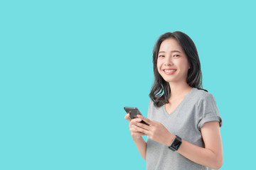 Young smiling Asian woman holding smartphone and wear smartwatch isolated on light blue background.