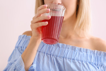 Woman drinking tasty pomegranate juice on light background, closeup