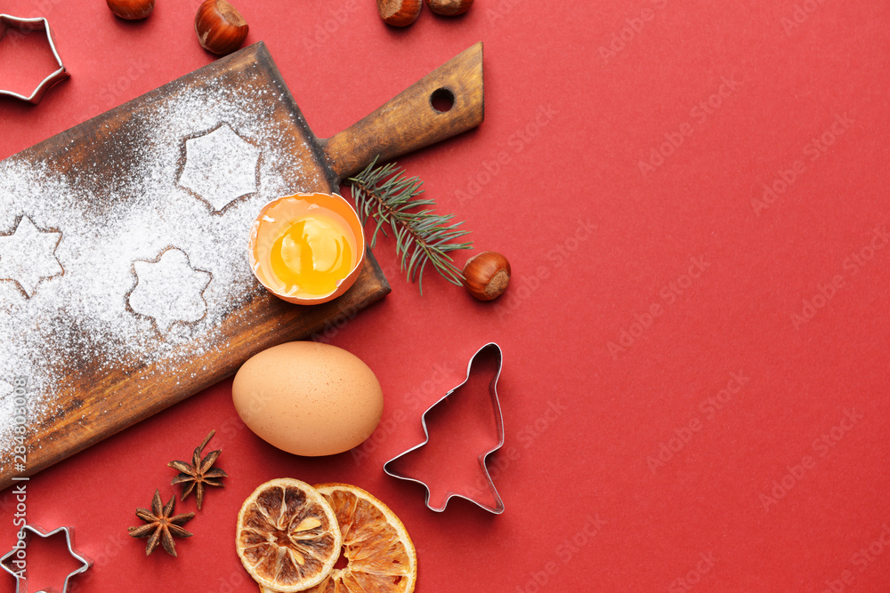 Wooden board with cookie cutters and ingredients on color background