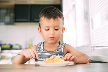 Wall Mural - a child in a t-shirt in the kitchen eating an omelet with sausage and tomatoes