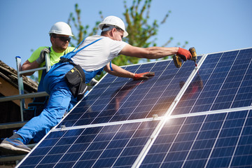 two workers technicians installing heavy solar photo voltaic panels to high steel platform. exterior