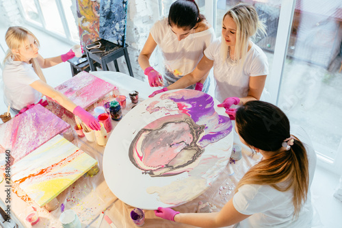 Cuadros en Lienzo Creative woman painter teach group of four female students creating fluid acrylic abstract painting in art therapy class, with table full of bottle with defferent paint colors