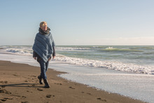 Mature Woman With Poncho That Walks On The Seashore In Autumn