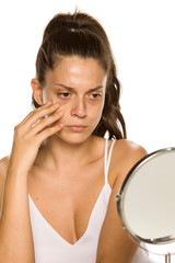 Poster - Worried young woman look at her self in the mirror on white background