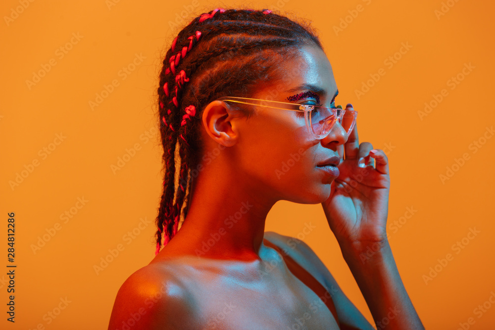 Beautiful young african naked woman posing isolated over yellow neon lights wall background