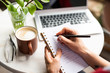 © pressmaster - Female hands holding notebook and pen while making working notes by table
