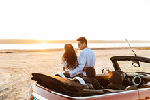 Photo From Back Of Attractive Multiethnic Couple Hugging Together While Standing By Car On Beach