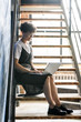 © pressmaster - Young woman with laptop looking at display while surfing in the net on staircase