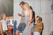 © snedorez - Photo of young parents, boy with phones in their hands and girl next to gray concrete wall outside