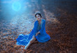 Young woman with the moon. Night autumn landscape. The Eastern Queen in a blue dress sits on the ground covered with fallen leaves in the moonlight. Tales of Shikhirizada 1001 nights. Art photography