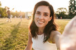 © Drobot Dean - Image of smiling middle-aged woman taking selfie photo while sitting on grass in summer park