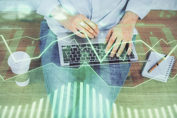 Double exposure of businessman's hands with laptop and stock market graph background. Concept of research and trading.