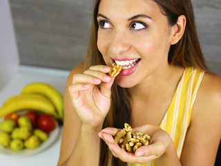 Wall Mural - Beautiful young woman smiling and eating walnuts at home. Close up from above looking to the side.