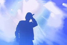 Silhouette Of Rap Singer Performing On Concert. Rapper Singing On Stage In Night Club. Hip Hop Music Poster Template. Blue Background With Cool Musician For Wallpaper Design